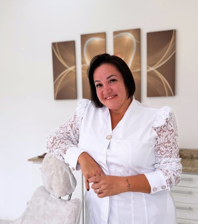 Dra. Daniela Bassani sorrindo, apoiada na cadeira odontológica do consultório em Encantado